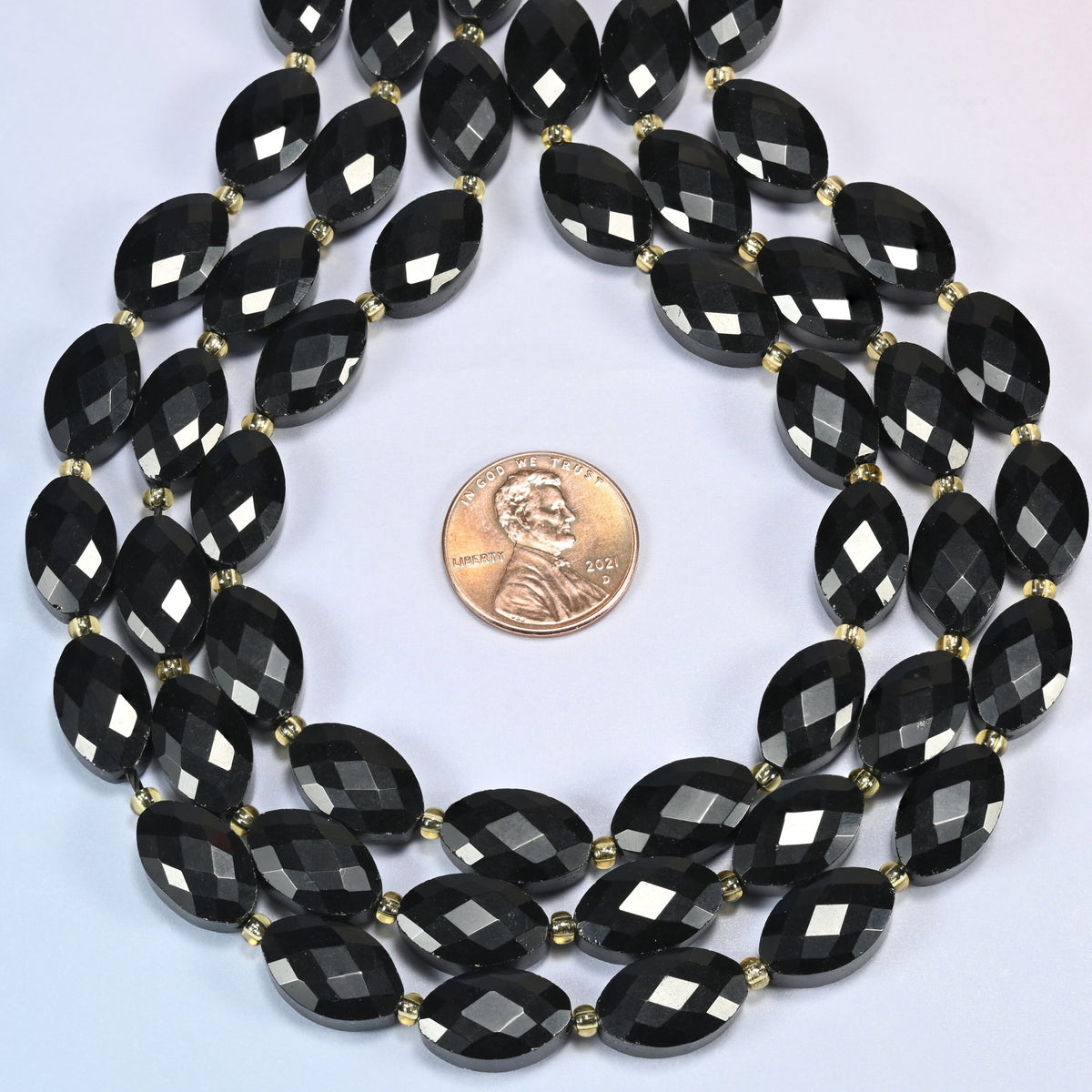 Black onyx faceted flat oval strands formed into a teardrop loop around a US penny for scale