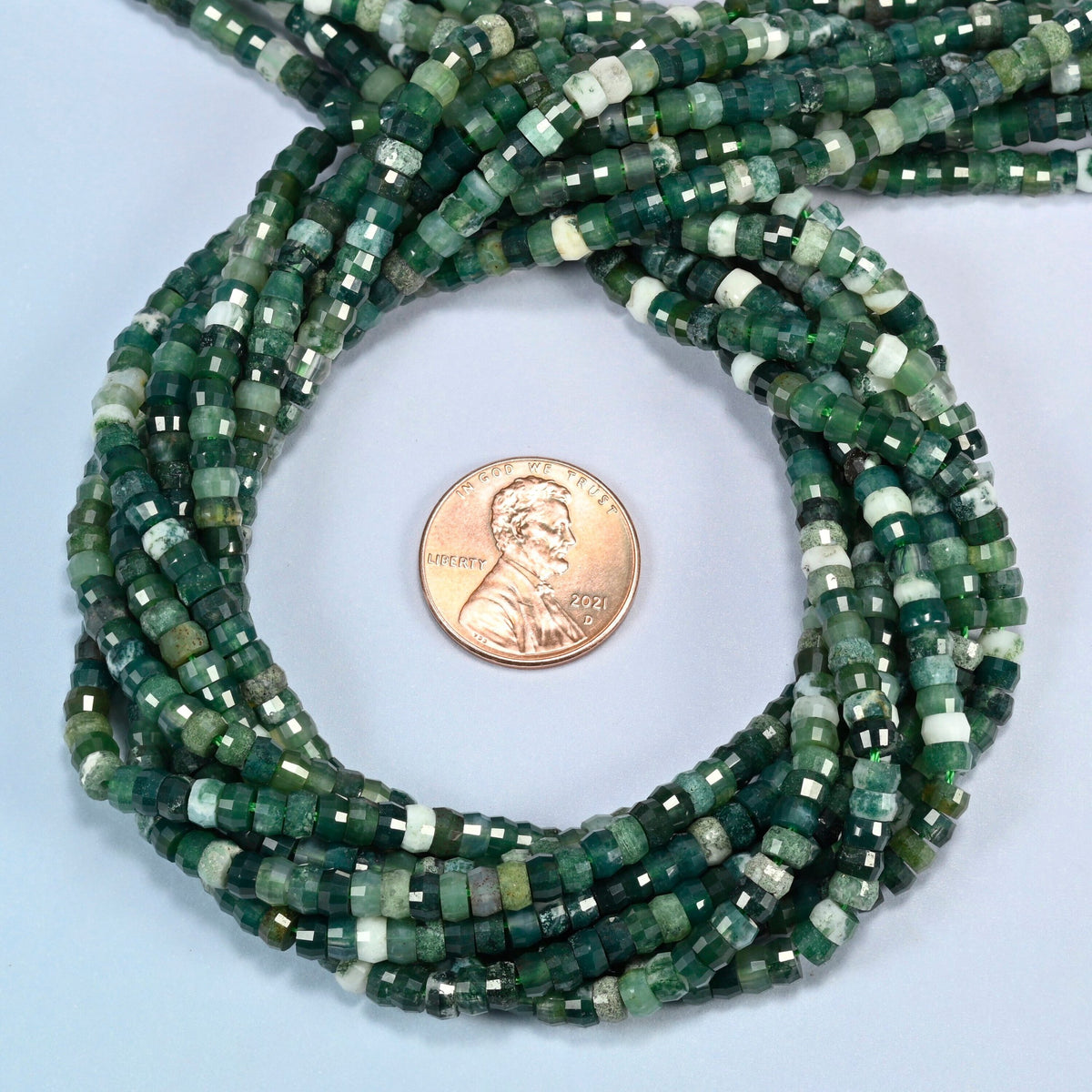 Moss agate faceted heishi disc beads 2x4mm coiled in a loop around a US penny for scale, close-up of the faceted disc shape