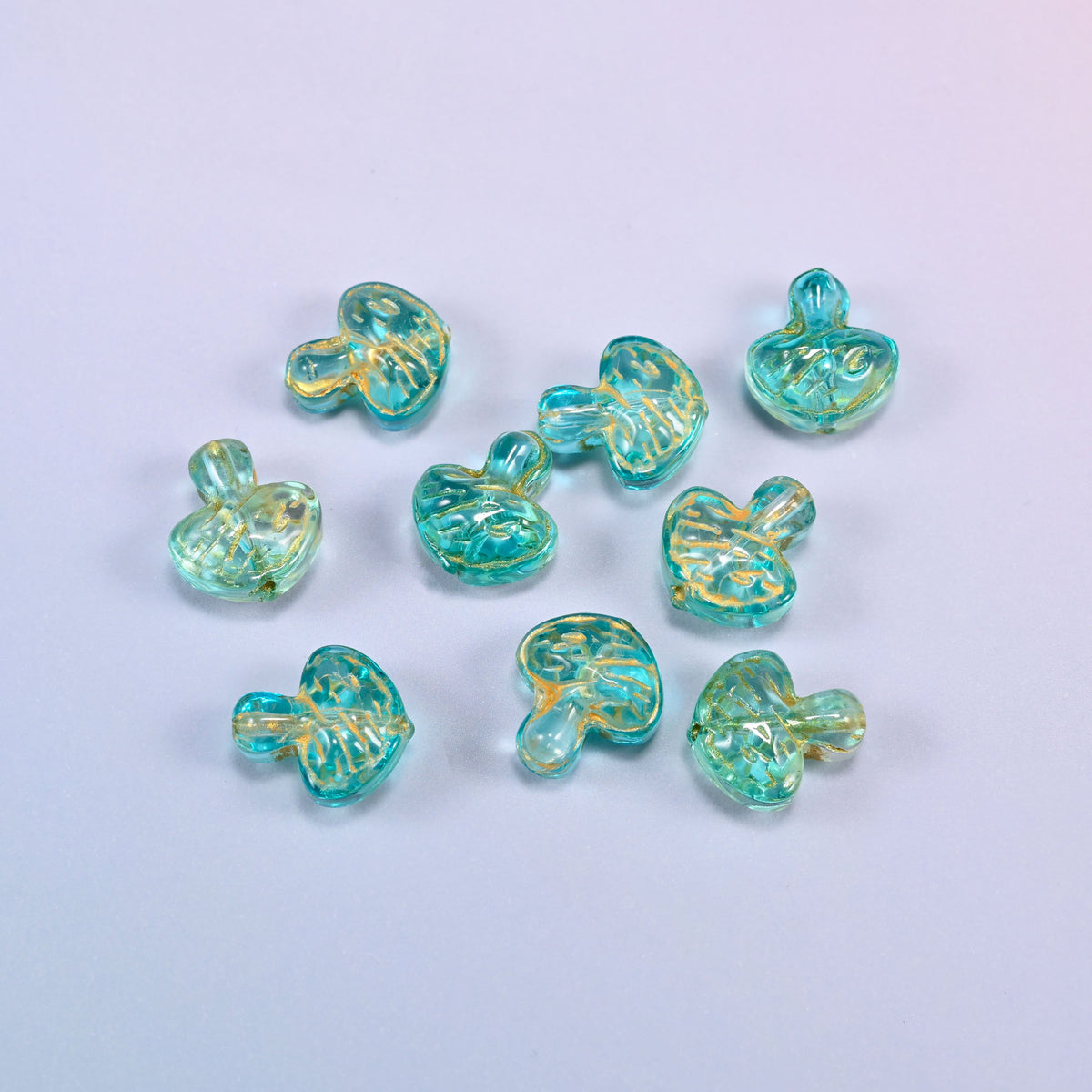 A scattered group of loose 13x12mm aqua gold flat mushroom glass beads, showing the gill lines under each cap.