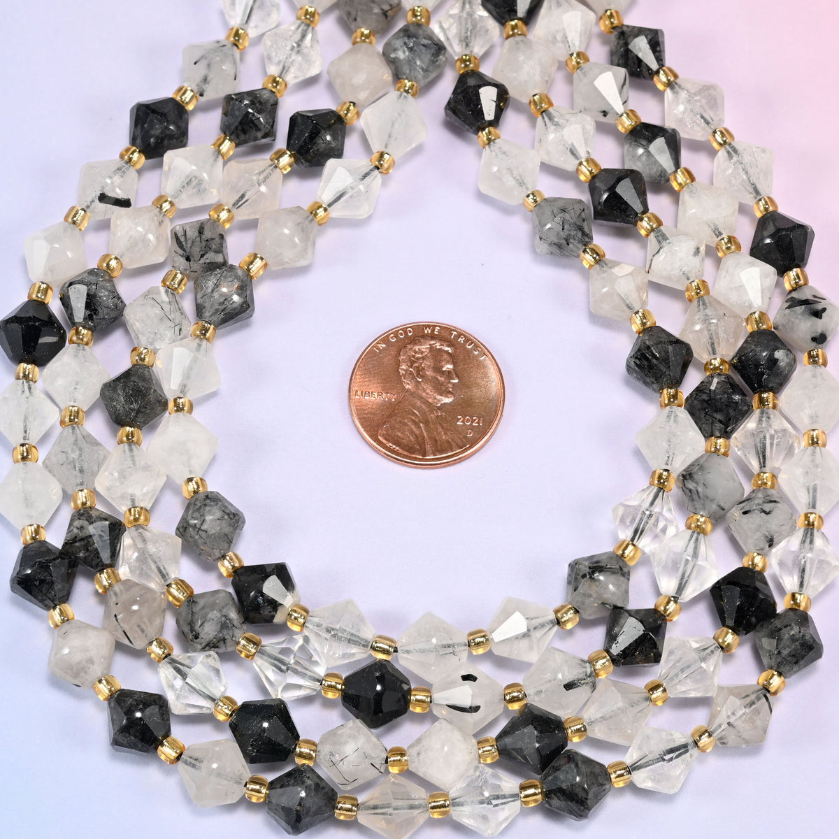 Black rutilated quartz bicone beads coiled into a ring, seen from above, facets catching the light across the coil.
