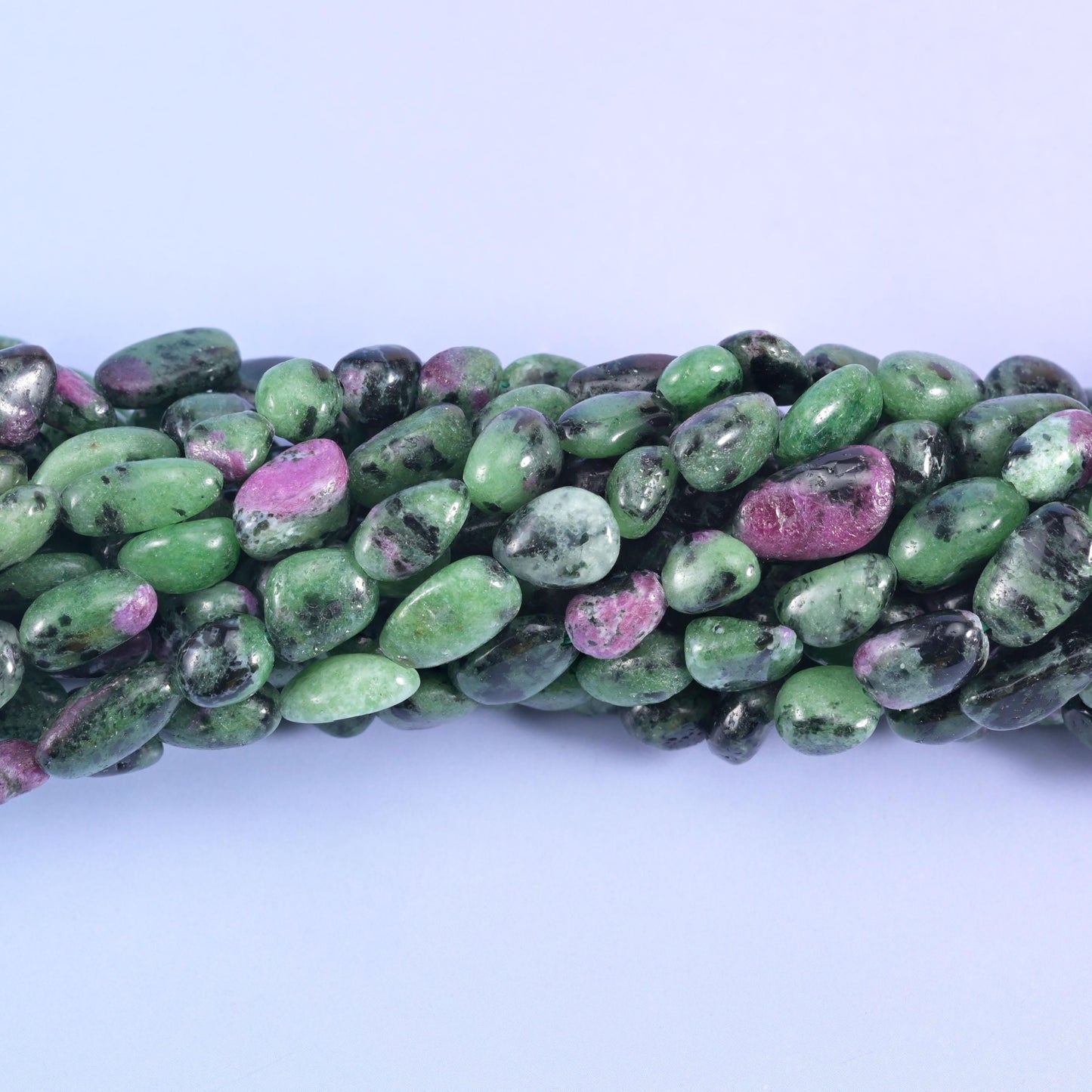 Smooth tumbled nuggets in bright apple green, streaked with charcoal-black hornblende and flecked with raspberry-pink ruby