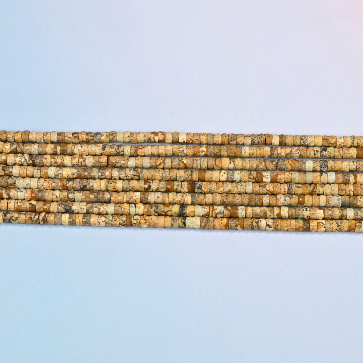 Several strands of picture jasper faceted heishi disc beads laid in straight rows