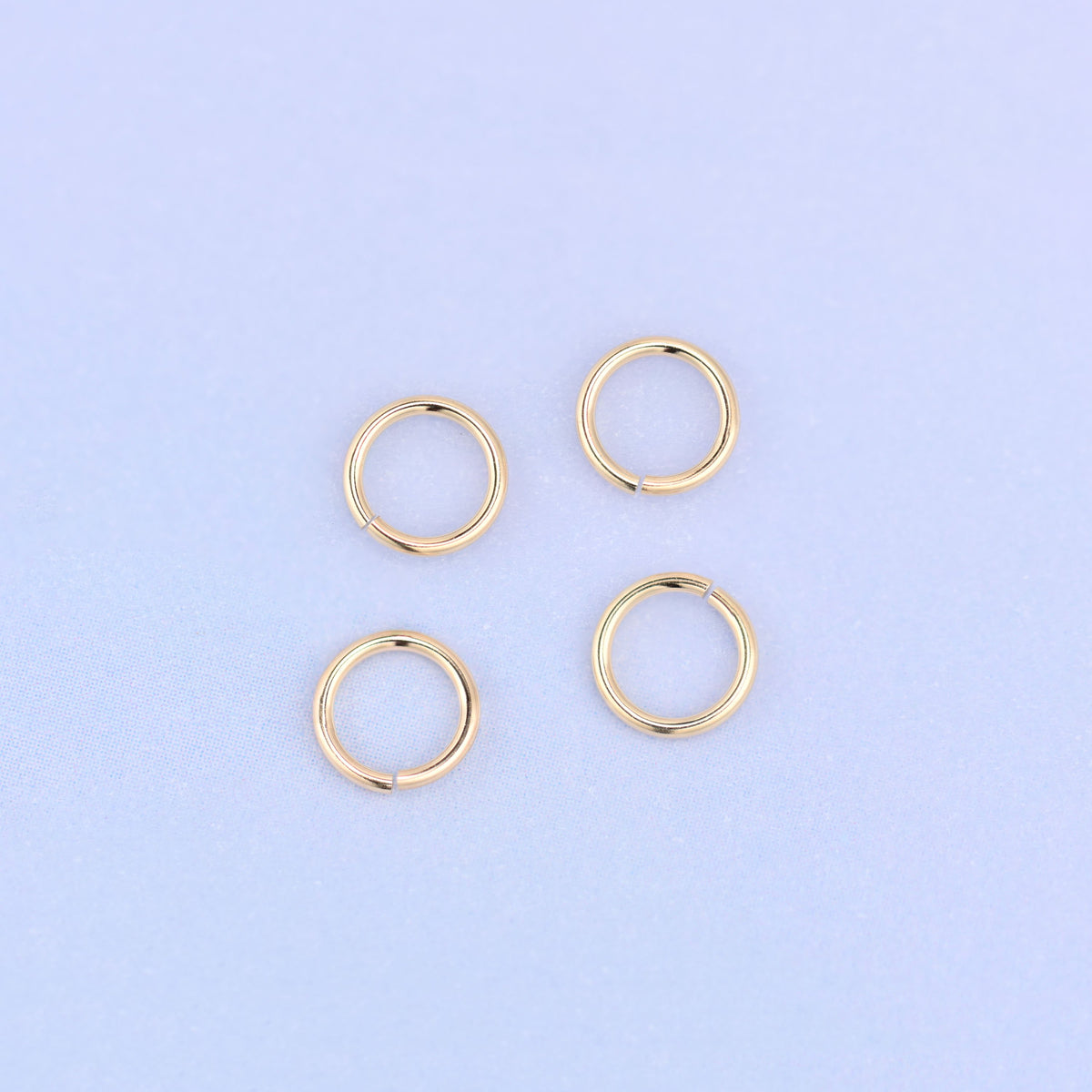 Four 14K gold filled open jump rings laid flat in a loose square, each 5mm ring turned so its opening sits at a different angle.