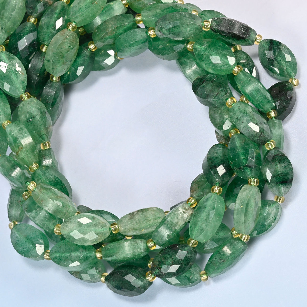 Green strawberry quartz faceted flat oval beads coiled into overlapping loops, whole strands of deep green stone