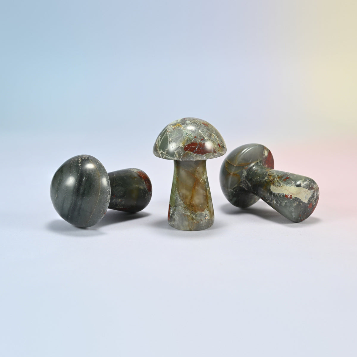 Three 2 inch African bloodstone mushroom crystal carvings shown standing and lying, gray-green with red and tan patches