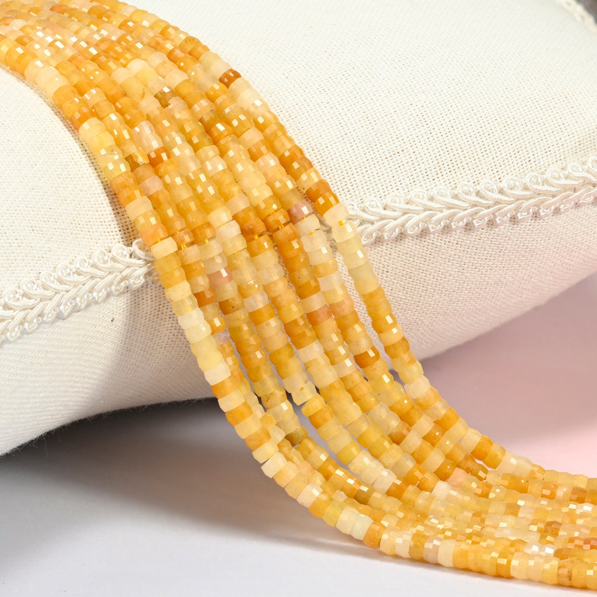 Gold Silk Jade faceted heishi disc beads 2x4mm, several strands draped over a white cushion