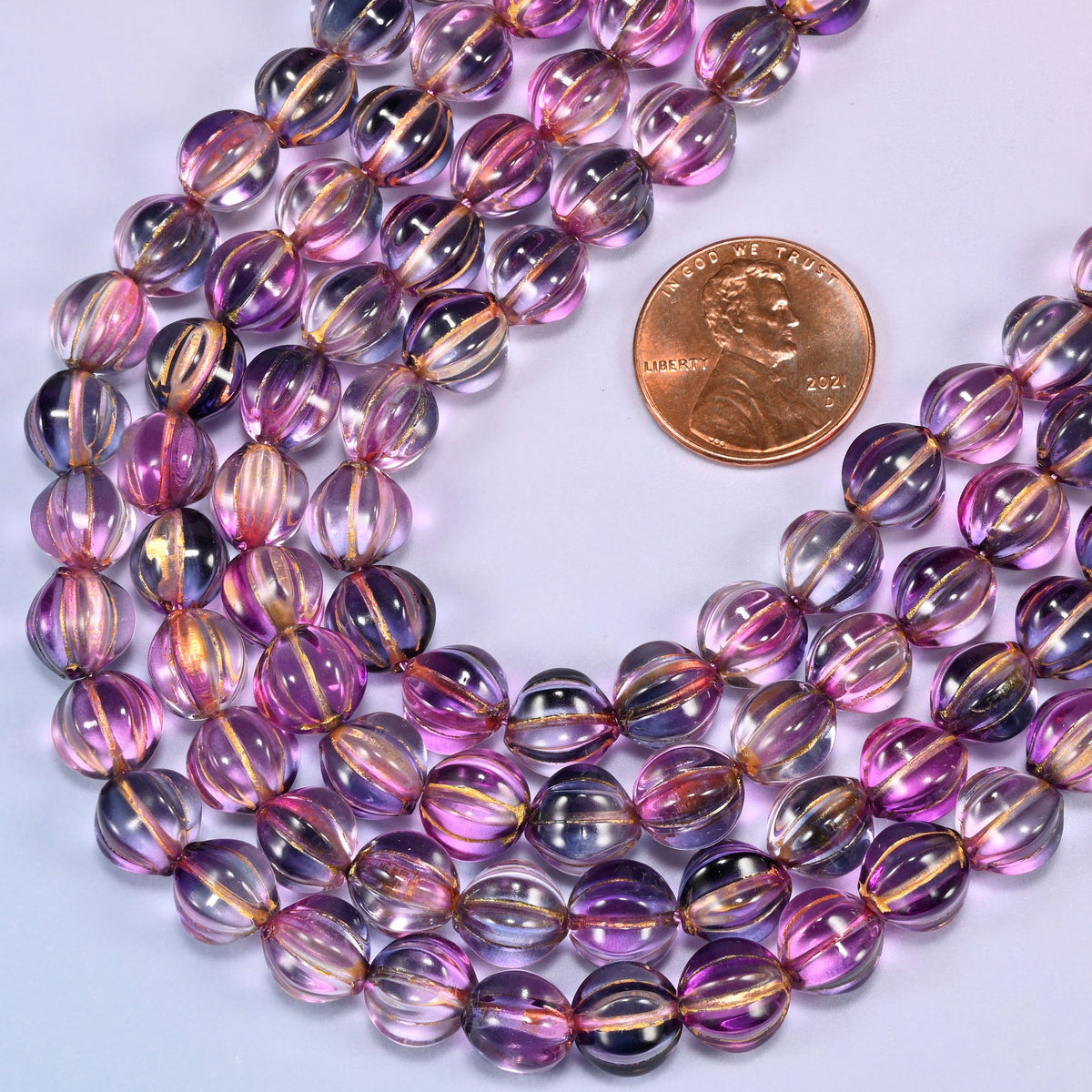 Pink blue gold pumpkin glass beads laid in a wide shallow bend, pink and blue-violet running together through the glass with a warm gold stripe down each rib.