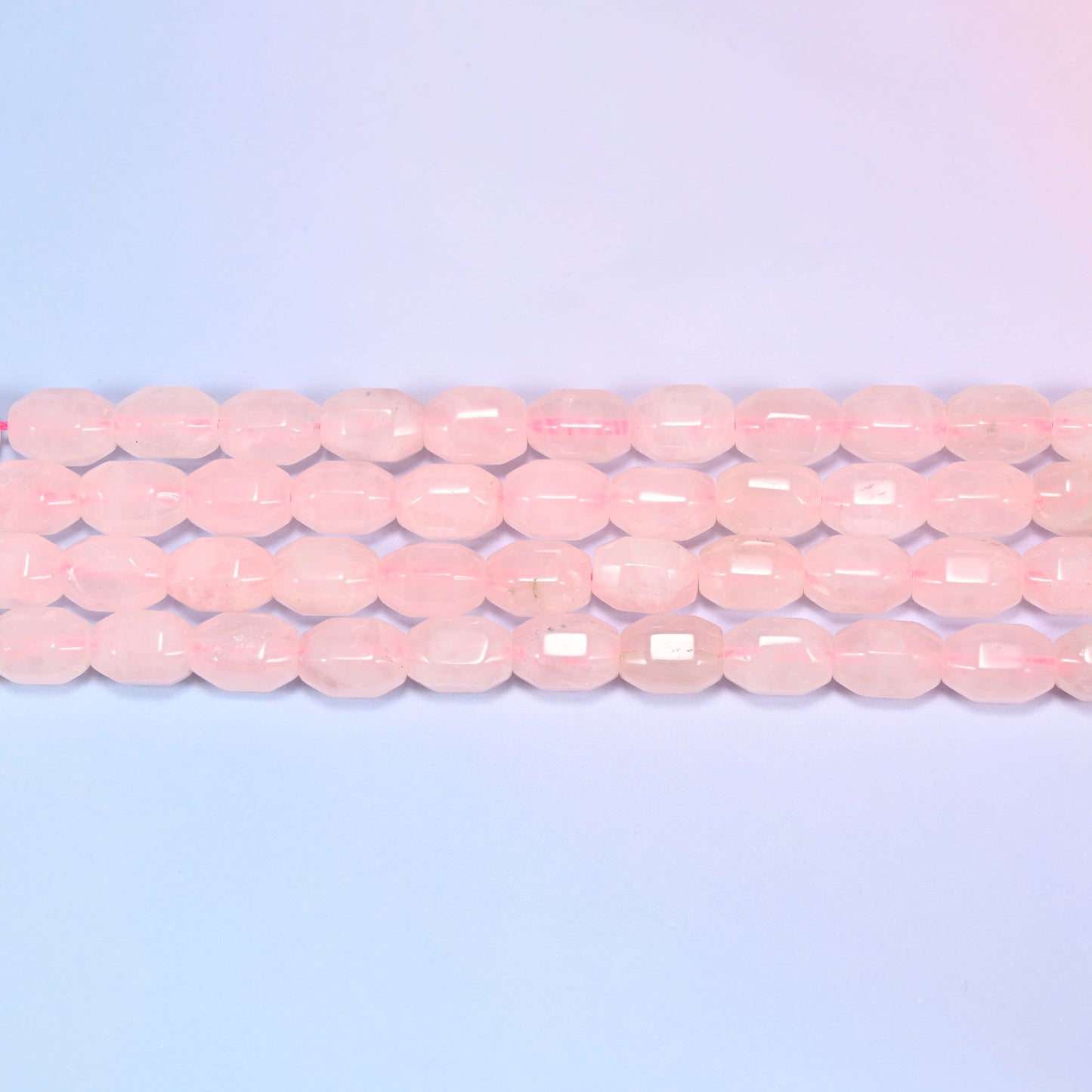 Close-up rows of Rose Quartz faceted barrel beads laid diagonally, showing the soft blush pink tone and facet cuts.
