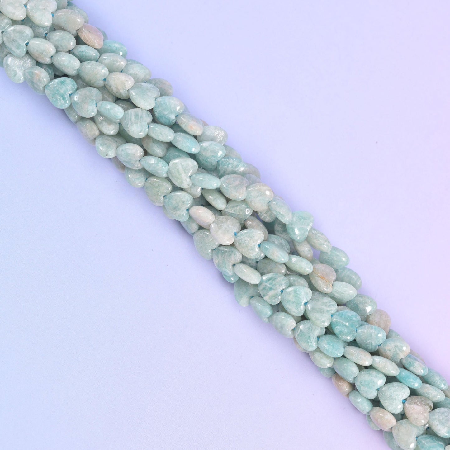 Diagonal run of pale blue Amazonite heart beads across a pastel backdrop