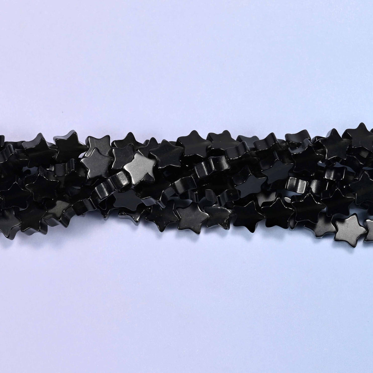 Small flat five-point stars cut from glossy jet black volcanic glass, with the odd bead throwing a silvery sheen across its face.