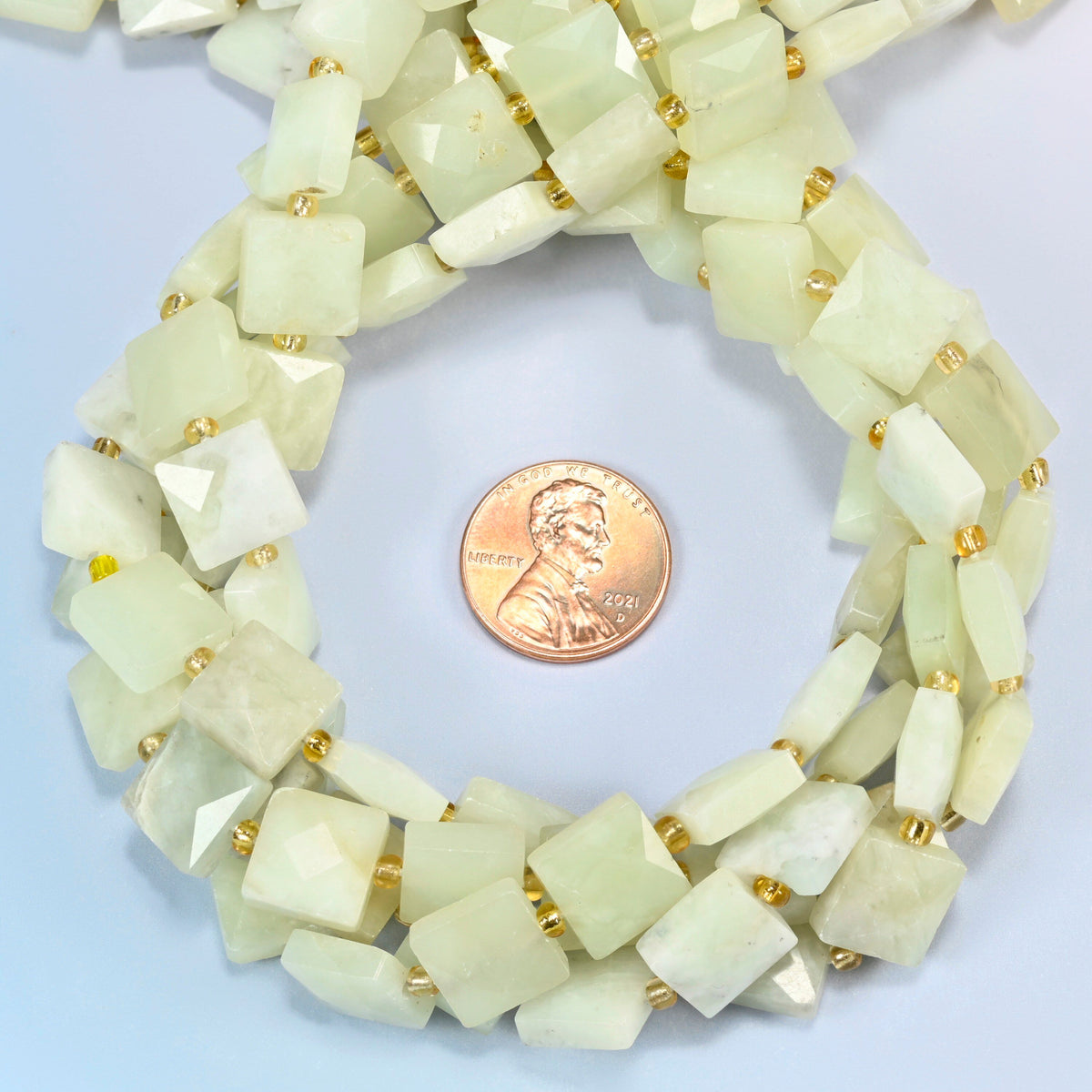 New Jade faceted flat square beads 10x10mm coiled in a loop around a US penny for scale, close-up of the faceted flat square shape