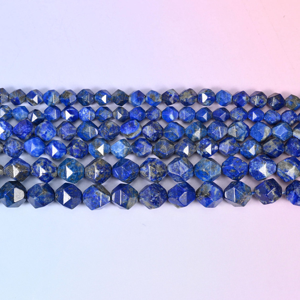 Blue Lapis Lazuli faceted beads in flat horizontal rows on a soft pink and lavender background, sold per 15.5 inch strand