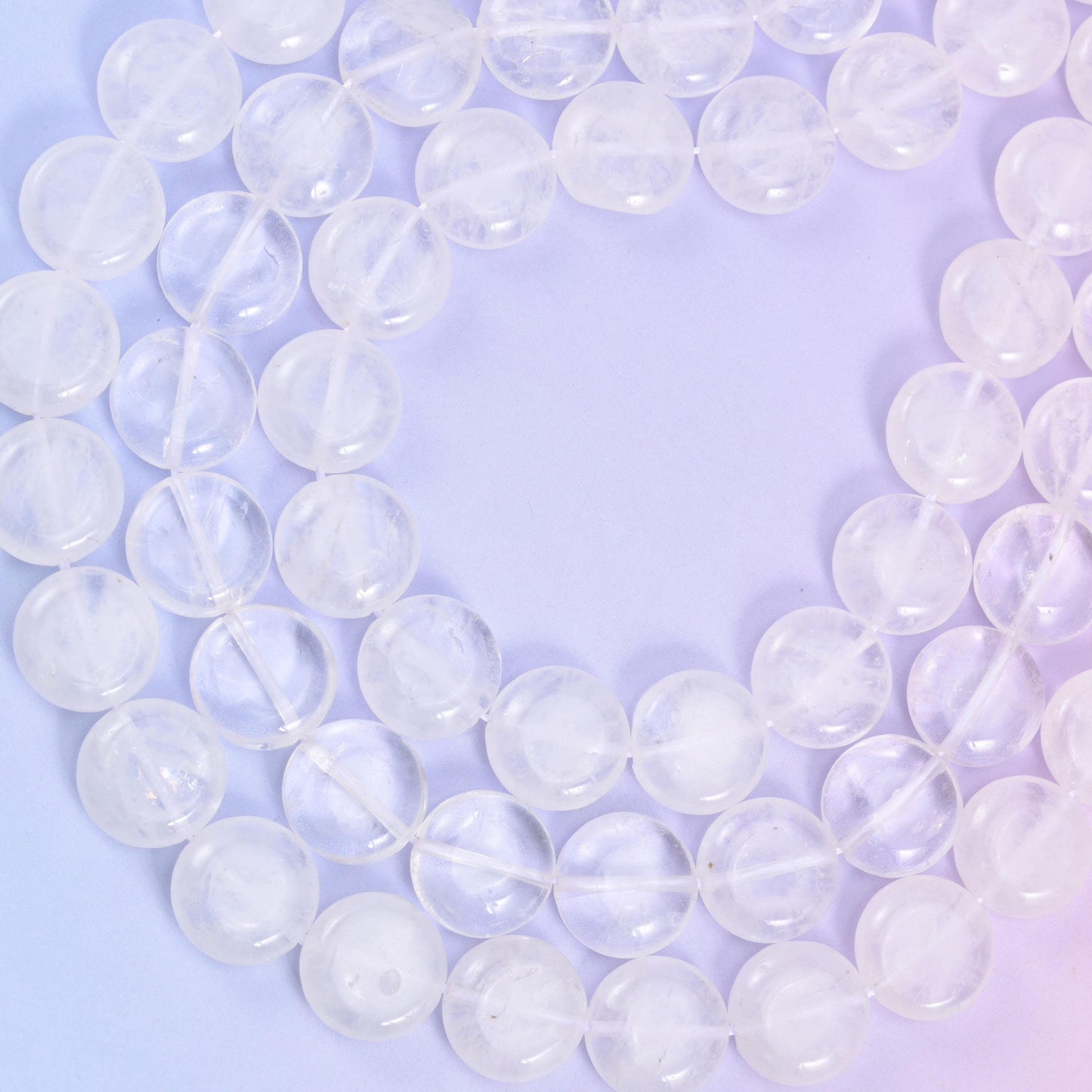 Two clear quartz strands crossing on a pale blue backdrop, polished coin edges catching light