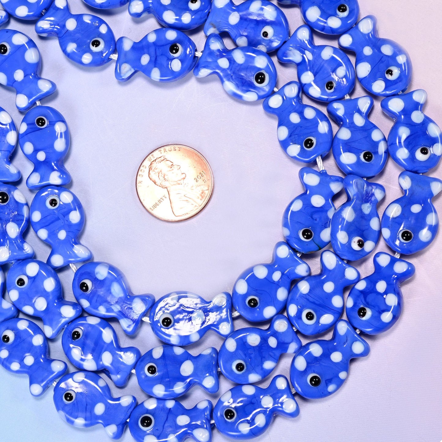 Solid royal blue lampwork fish, opaque rather than see-through, covered in bold white dots with a white-ringed black eye on each side. High contrast, and easy to spot in a busy charm cluster.