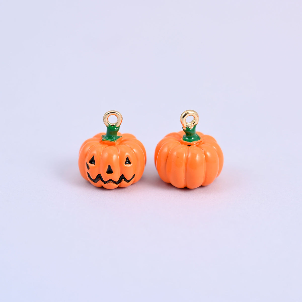 Enamel pumpkin charms shown front and back, one with the jack o lantern face and one showing the plain ribbed pumpkin body.