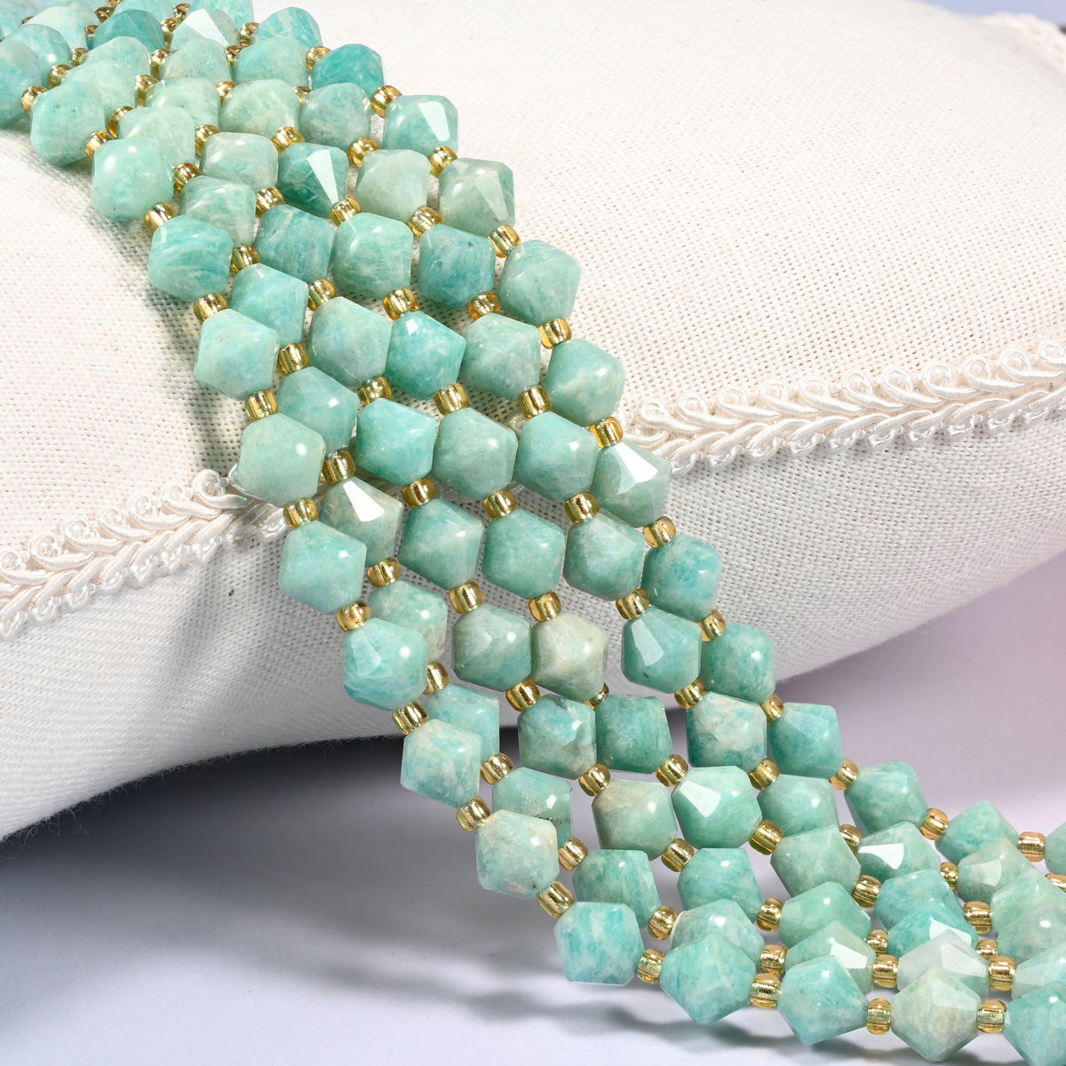 Green Amazonite faceted bicone beads 8mm with gold-tone spacers, strand draped over a woven cushion trim