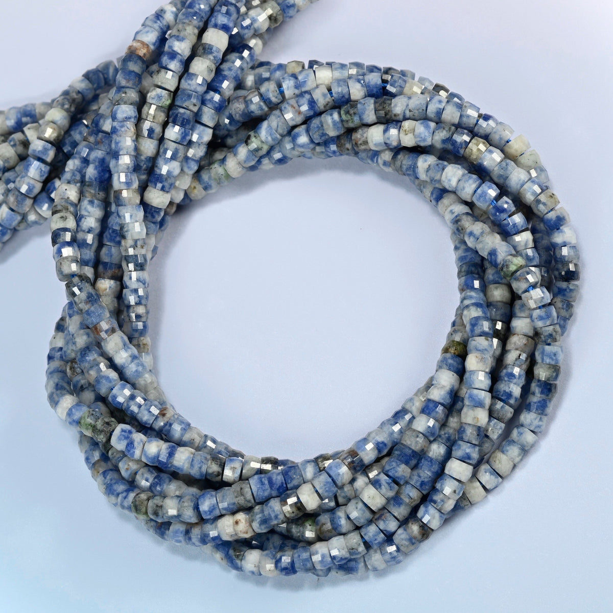Blue spot jasper faceted heishi disc beads coiled into overlapping loops, whole strands of speckled blue and white stone