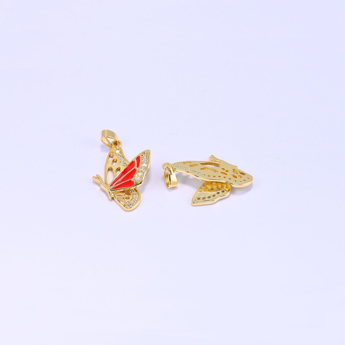 Flying butterfly charm pendant standing upright beside a second piece lying flat on its back, revealing the plain gold underside and cut out wing panels.