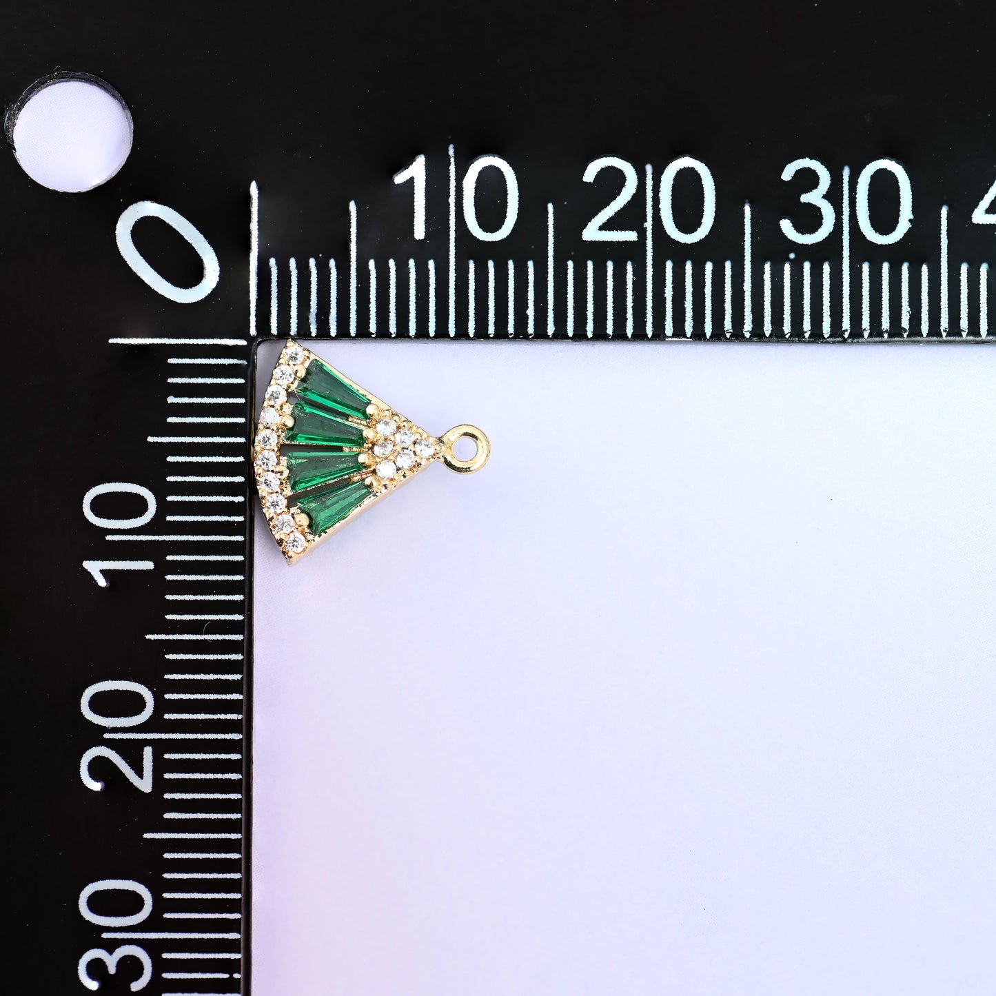 Small gold charms, one green fan charm measured against a millimetre ruler