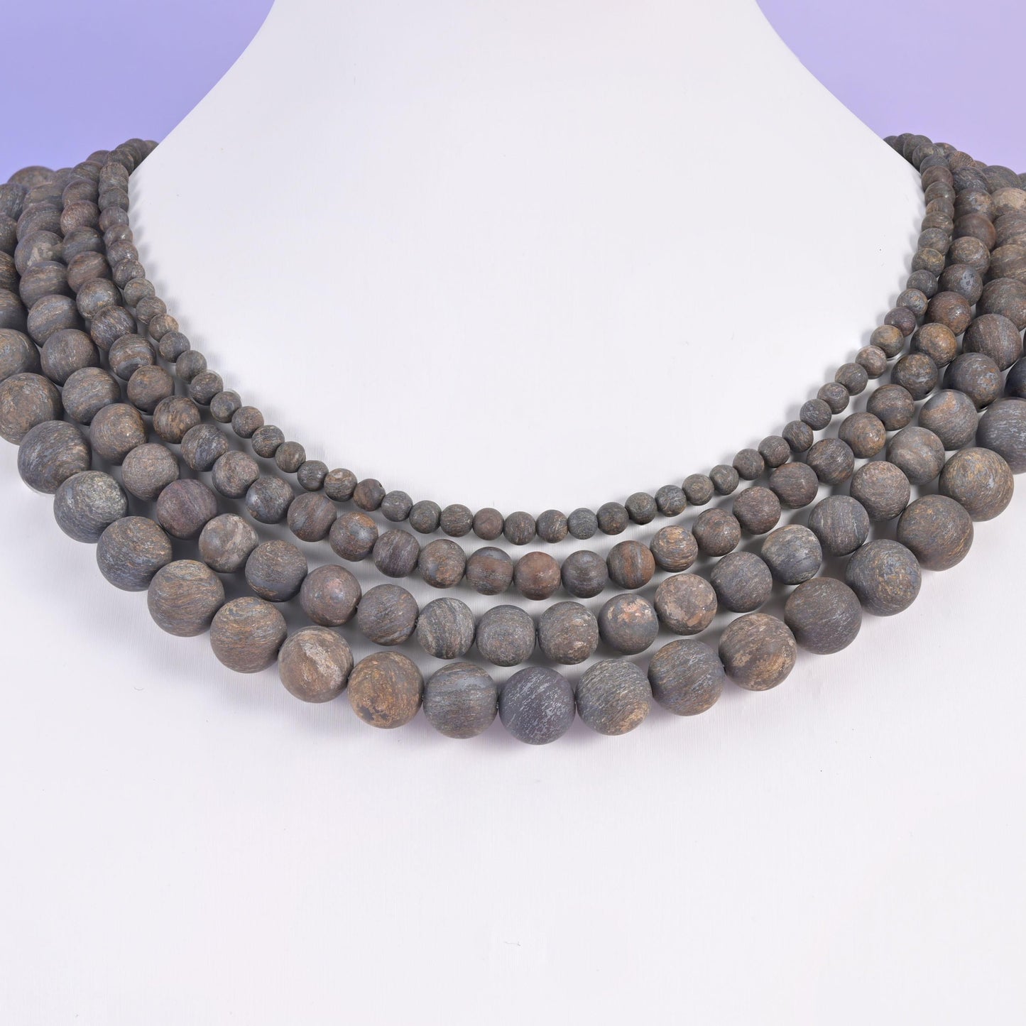 Bronzite matte rounds layered on a white display bust, four rows sitting close at the collarbone