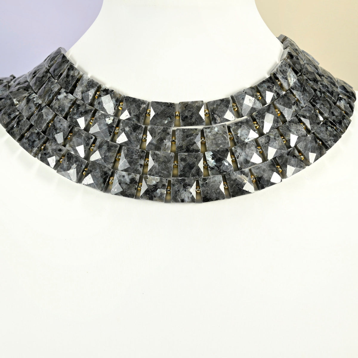 Natural black labradorite faceted flat square strands arranged as a layered collar on a white display bust, dark gray beads across the neck