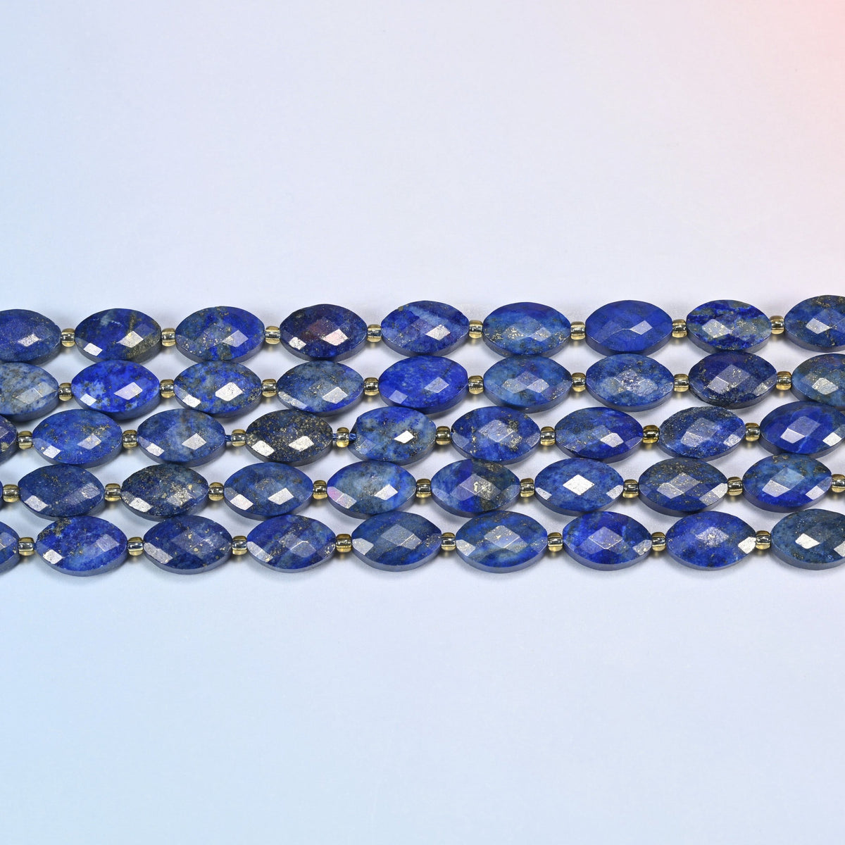 Several strands of lapis lazuli faceted flat oval beads laid in straight rows with gold seed bead spacers