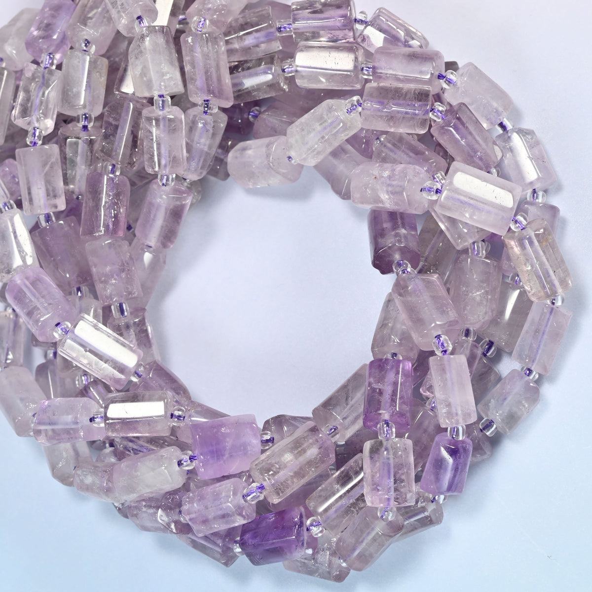 Lavender amethyst faceted tube beads coiled in overlapping loops, washed lilac and frosted white tubes stacked close.