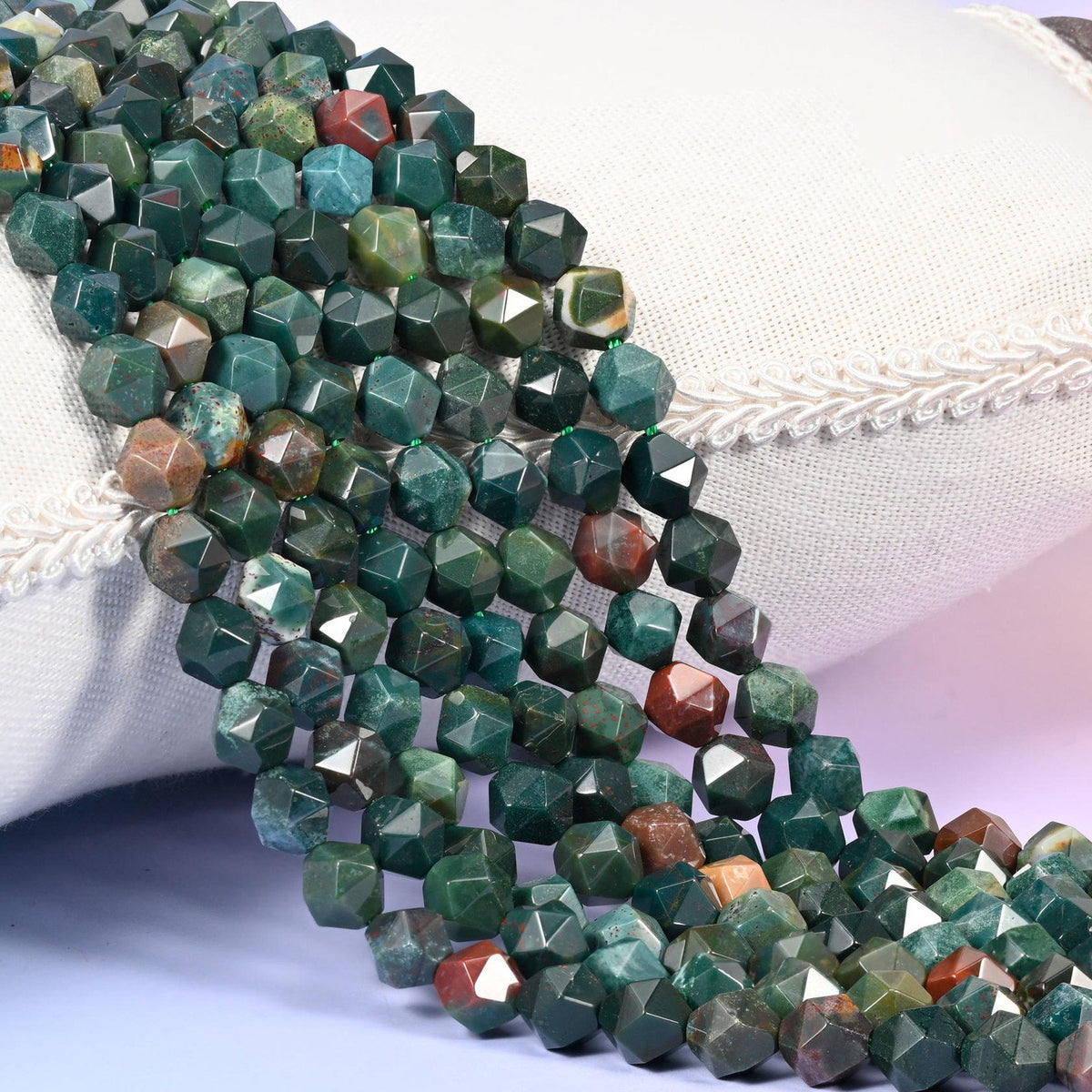 Indian Bloodstone diamond star cut beads, strands laid over white fabric, dark green stone with rust and red-brown beads mixed through