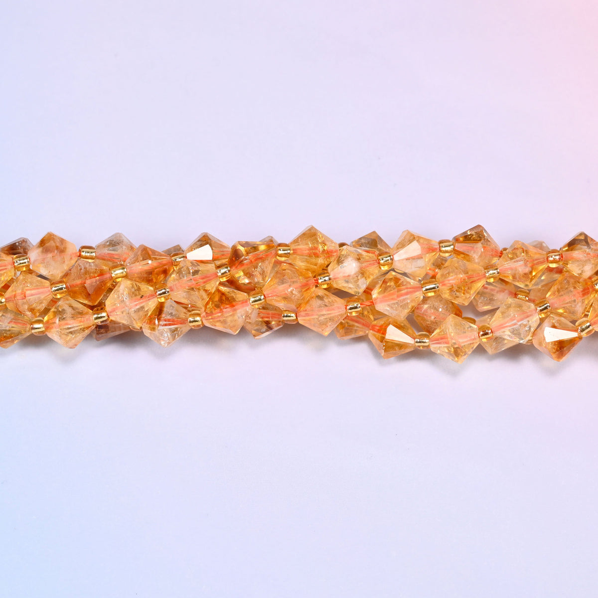 Citrine bicone beads shown as a single strand laid straight across, some beads paler and clearer, others a deeper orange.