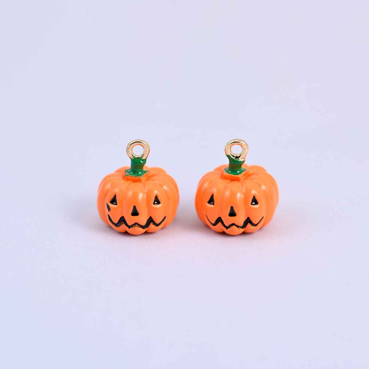 Two enamel pumpkin charms side by side, both showing the black jack o lantern face on the orange enamel body.