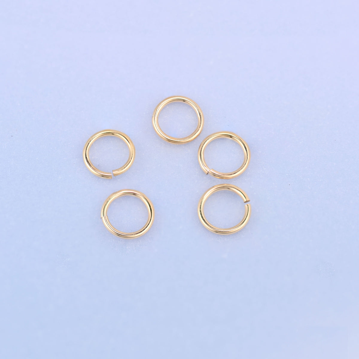 Five 14K gold filled open jump rings arranged in a ring, each split turned outward so the opening in the 5mm wire loop is easy to see.