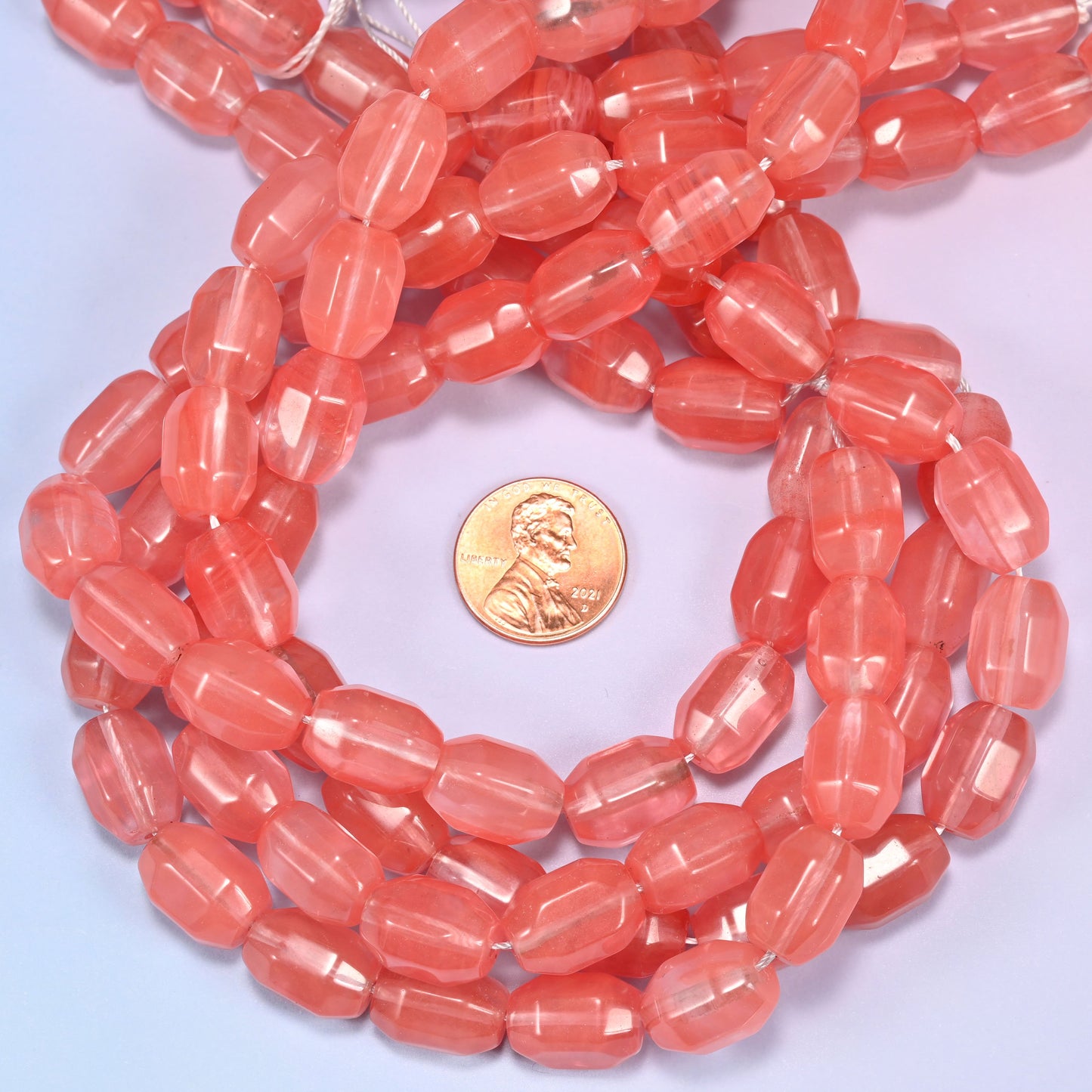 Close-up circular coil of faceted glass barrel bead strands with a penny in the center for size comparison.