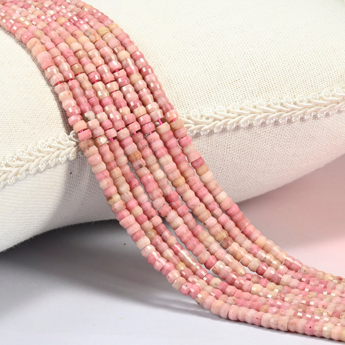 Pink rhodonite faceted heishi disc beads 2x4mm, several strands draped over a white cushion