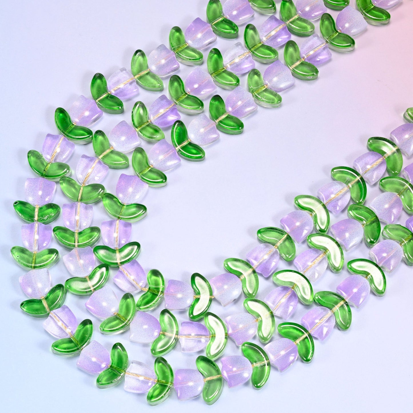 Close-up of tulip and leaf glass bead strands coiled in a tight spiral pattern on a lavender background.