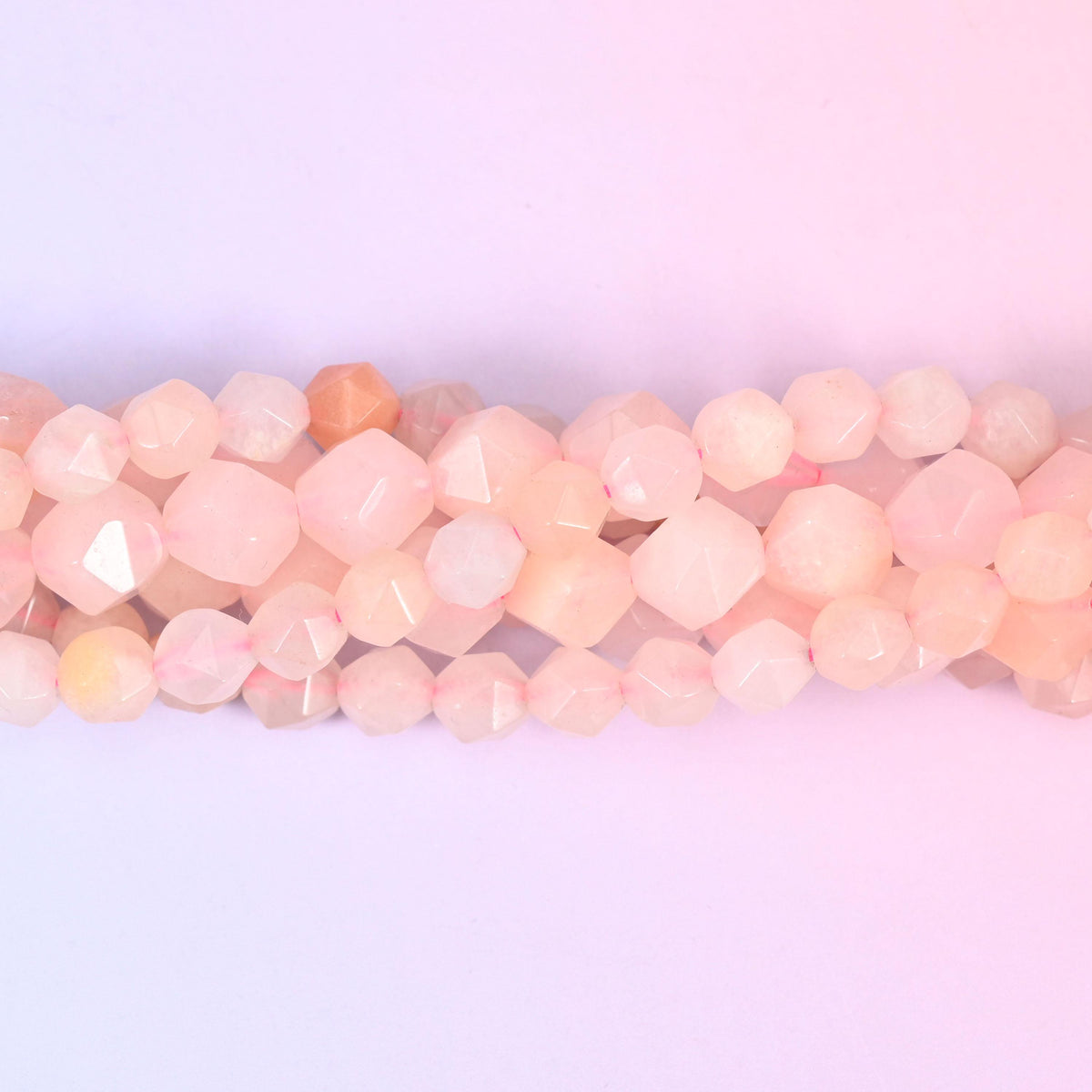 Pink Aventurine faceted beads close up in a single row, flat triangular star cut planes over blush pink and peach