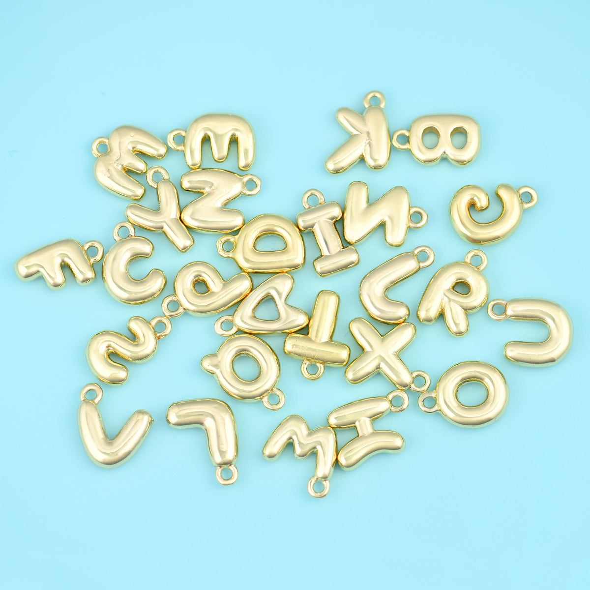 18K gold plated letter pendants in a loose pile, showing the full A to Z alphabet and the satin gold finish.
