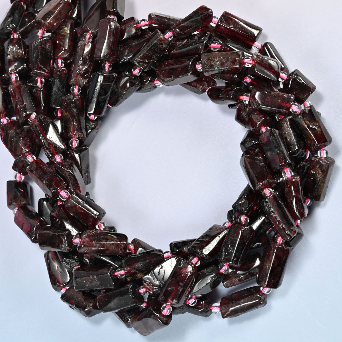 Red garnet tube beads coiled into overlapping loops, whole strands of deep cherry red stone