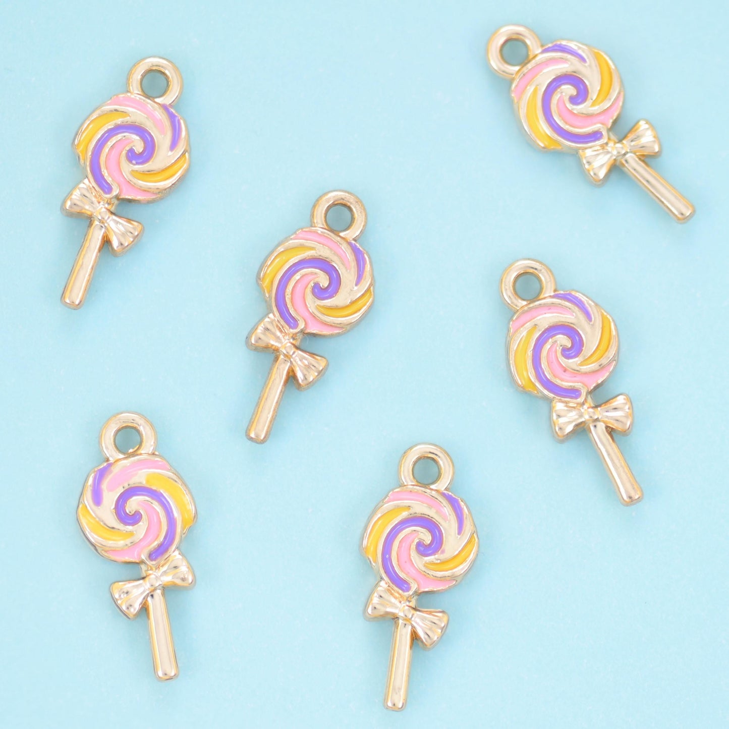 A flat little lollipop with the candy swirl painted in pastel enamel between fine gold lines — soft pink, buttercream,…