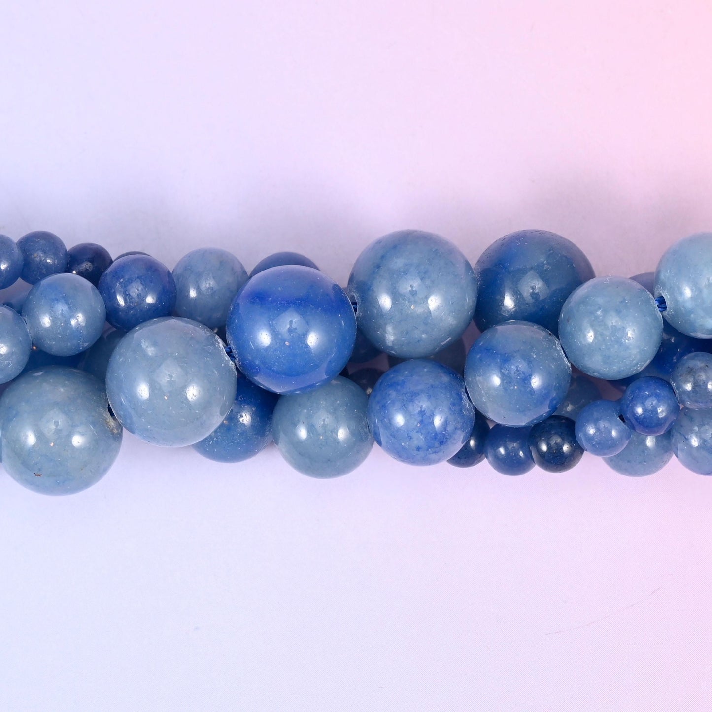 Denim blue rounds that run from pale powder to deep ink across a single strand, some beads flecked with darker navy, all polished smooth and evenly glossy. Straightforward