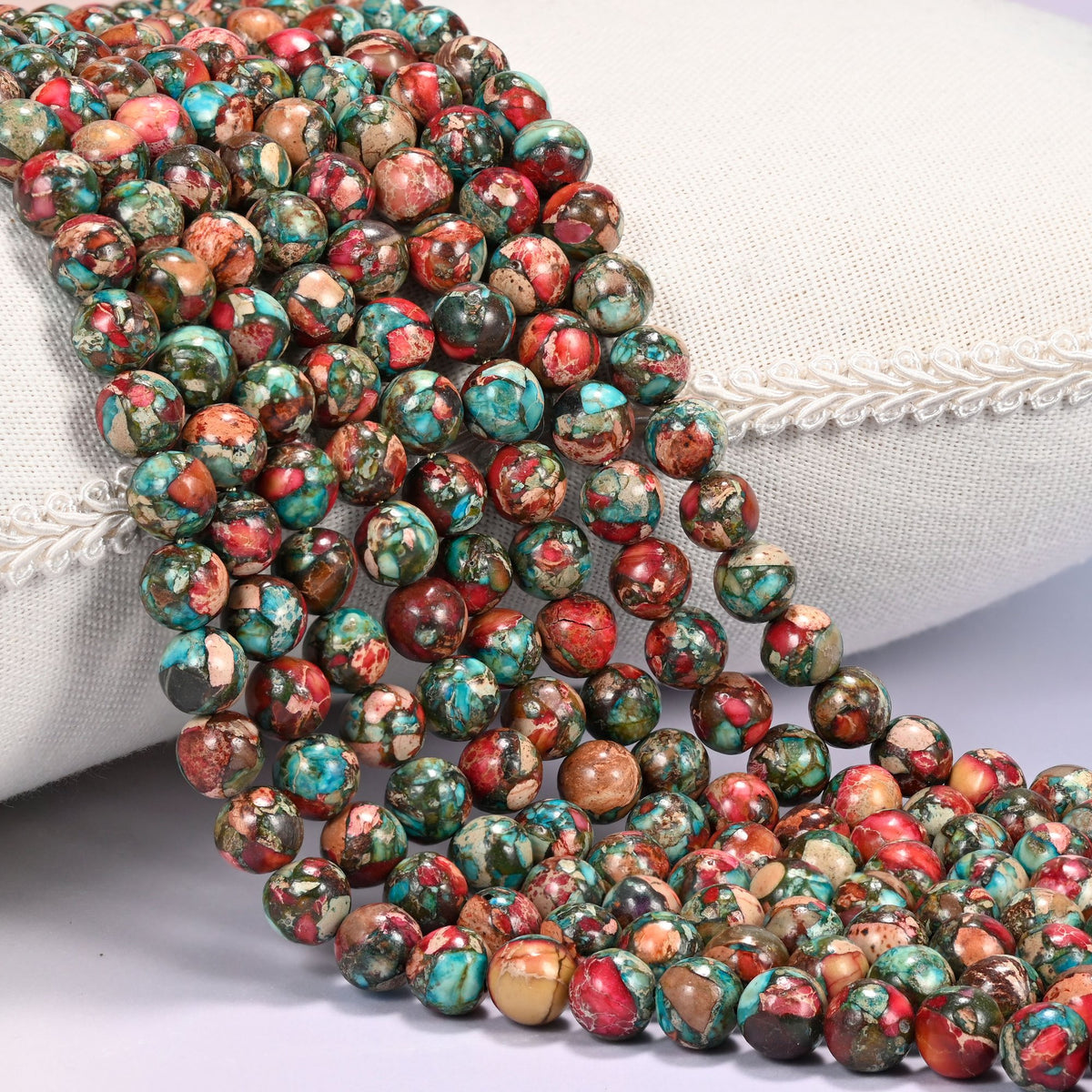 Red sea sediment jasper smooth round beads, several strands draped over a white cushion.
