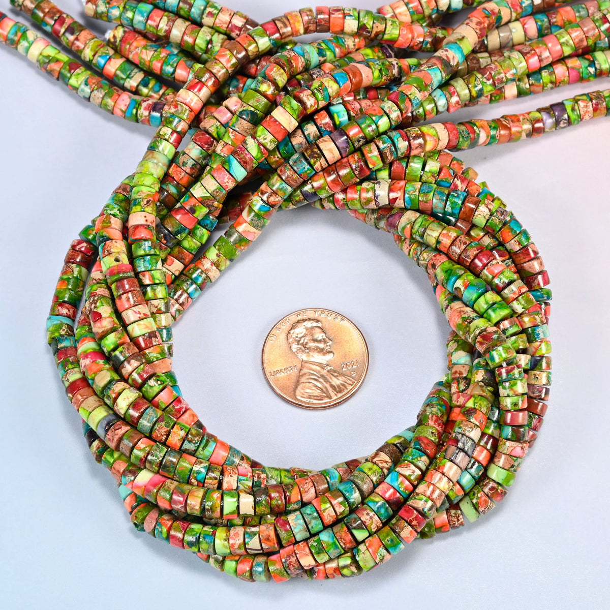 Dyed blue green sea sediment jasper heishi disc beads 2x4mm coiled in a loop around a US penny for scale, close-up of the thin disc shape