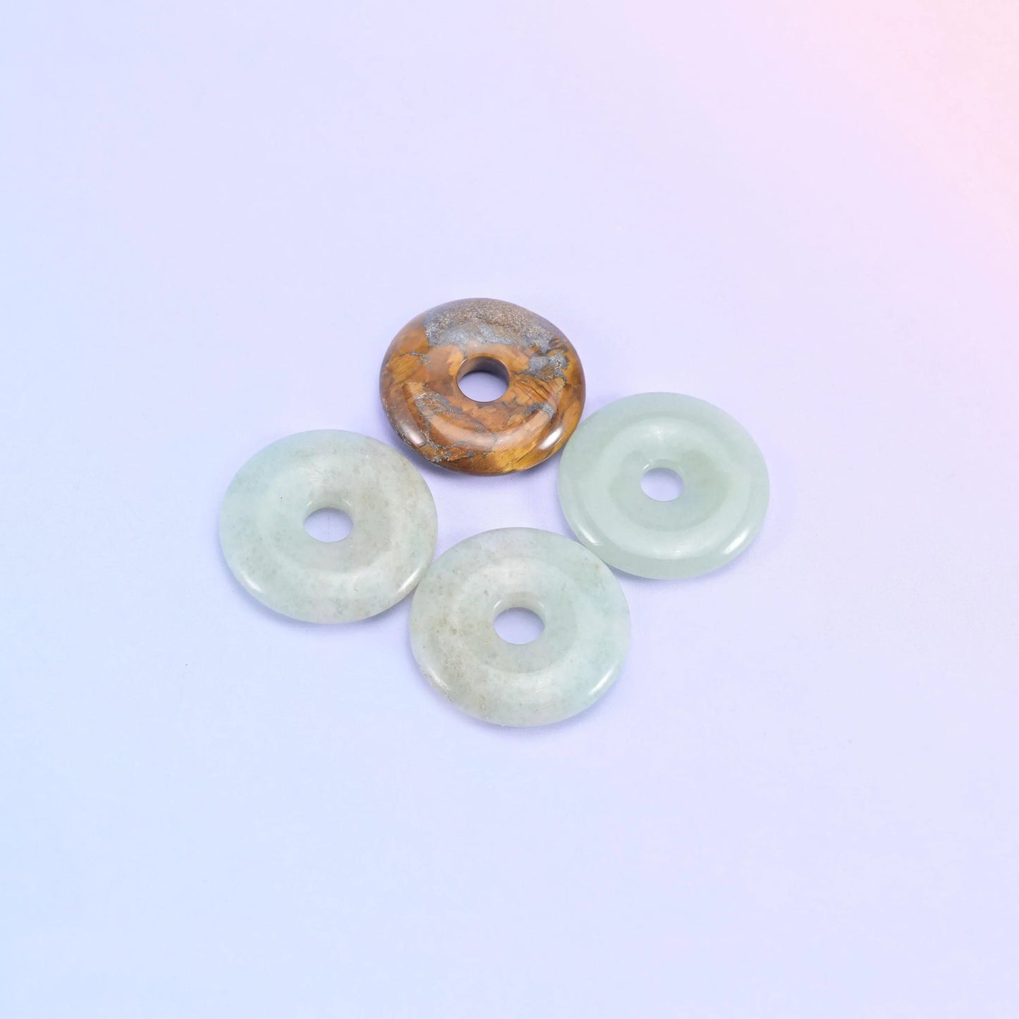 Three pale green donuts with one banded tiger eye donut resting on top