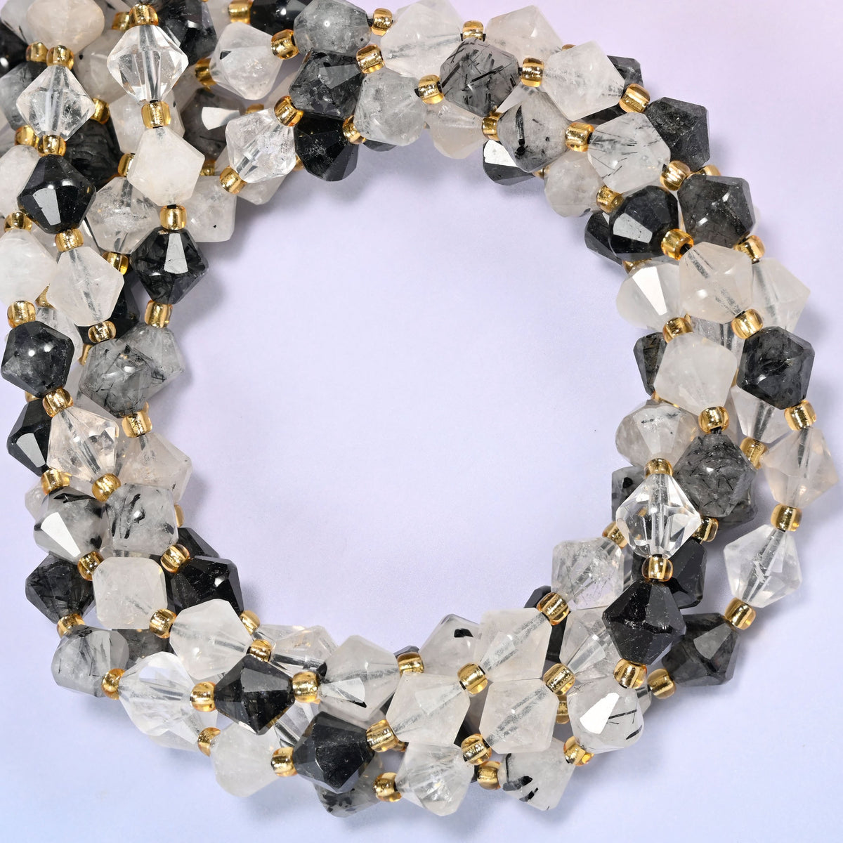 Black rutilated quartz bicone beads coiled into a round ring of several strands, clear, smoky and near-black beads mixed along the strand.