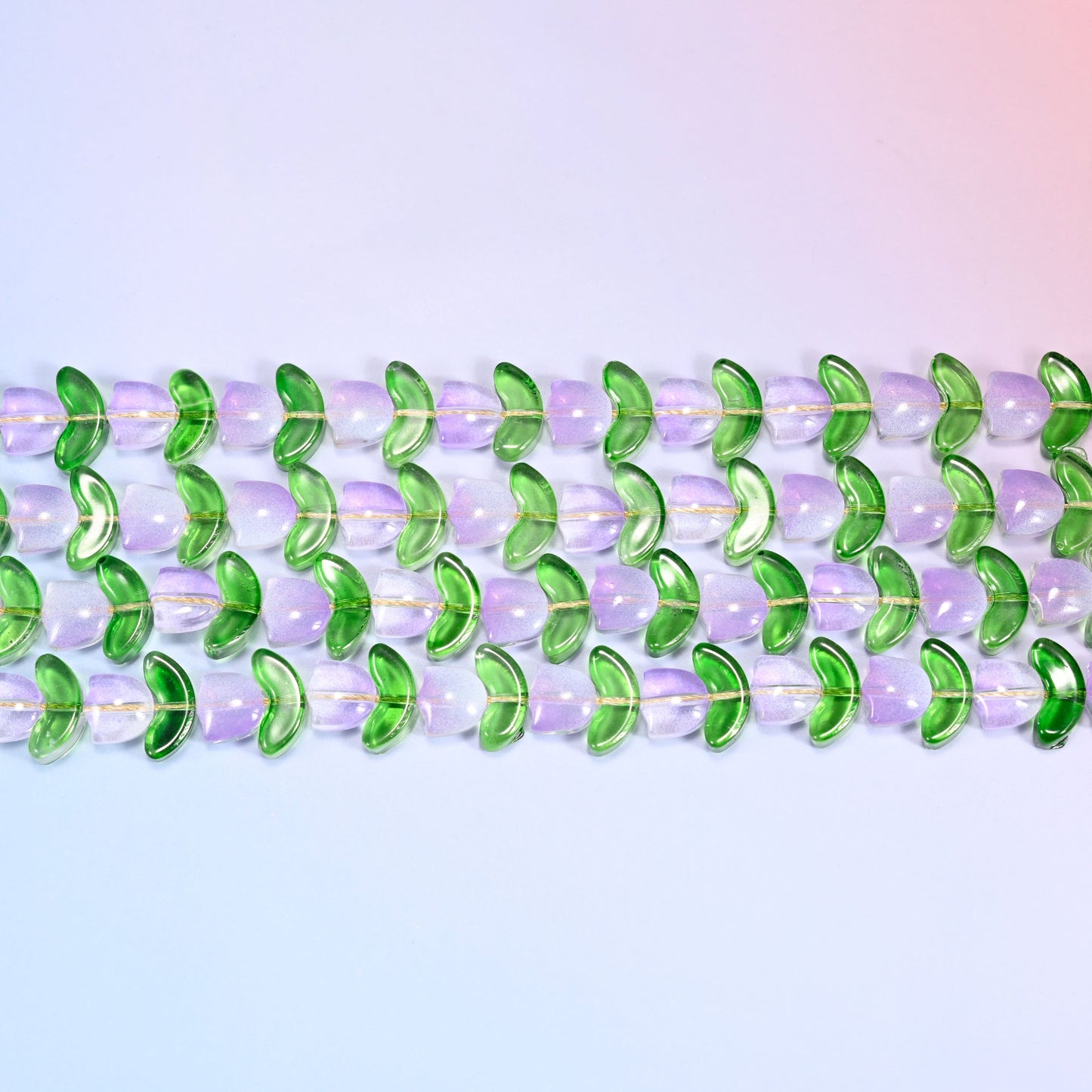 Close-up macro view of lavender tulip and green leaf glass beads in a dense repeating row pattern on a lavender and pink gradient background.