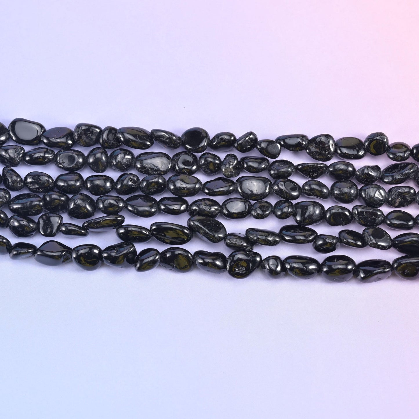 Rows of glossy black tourmaline nuggets on a pale lavender background