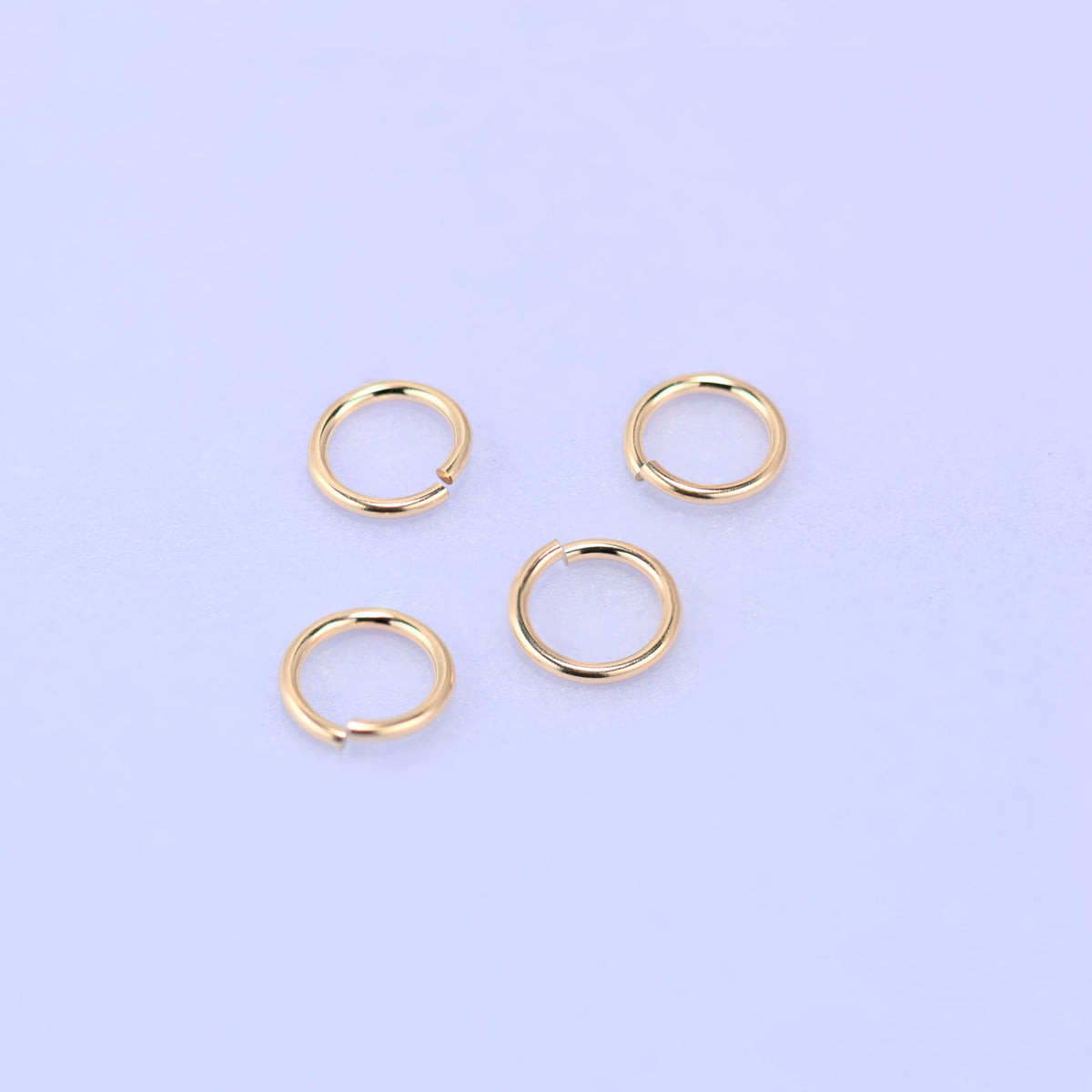 Four 14K gold filled open jump rings scattered loosely, the even round shape and consistent 5mm diameter visible across all four.