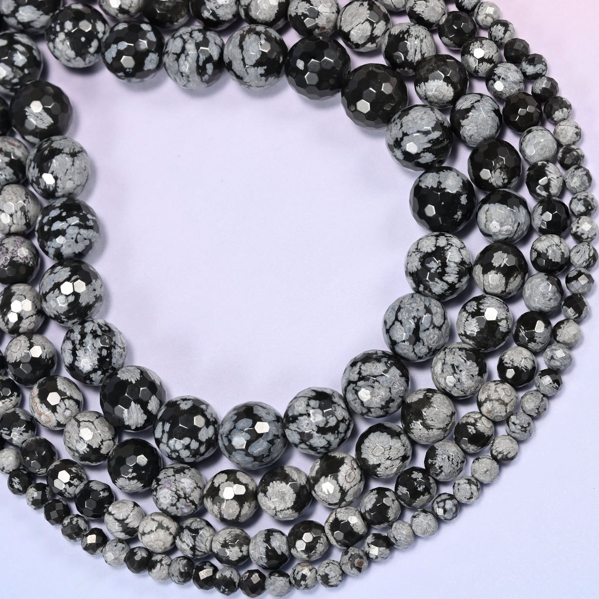 Snowflake Jasper faceted round bead strands coiled into a rounded loop, showing the stone's black background with gray snowflake-like mineral spots.