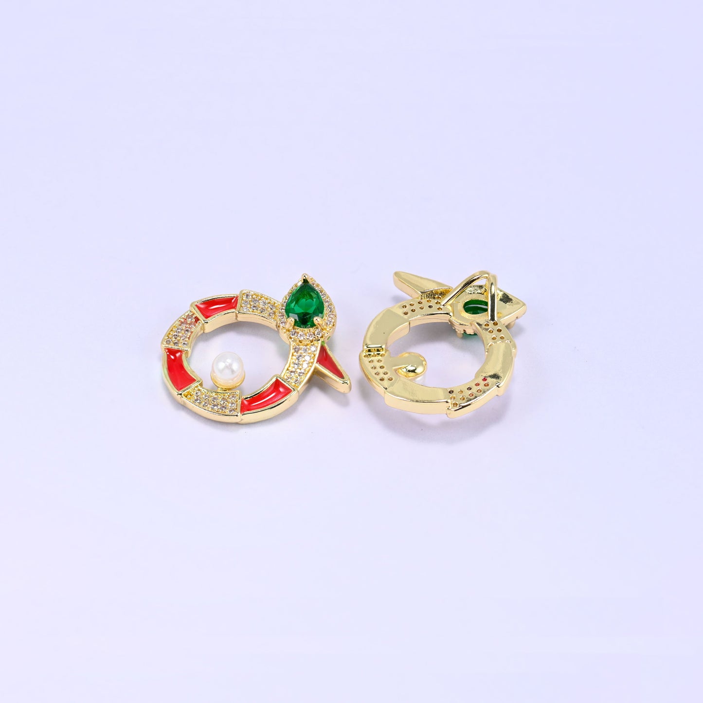 Round snake charm face and reverse laid at an angle, the red enamel and pearl front beside the smooth gold back of a second charm.