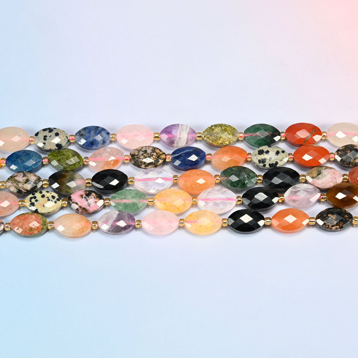 Several strands of assorted gemstone faceted flat oval beads laid in straight rows with gold seed bead spacers