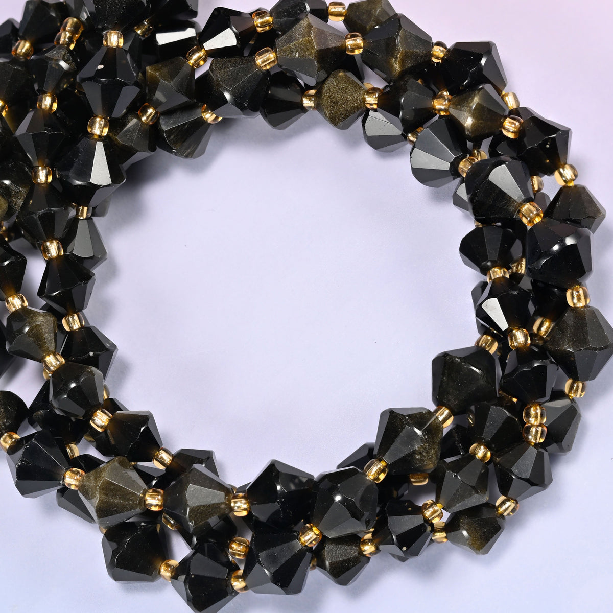 Gold obsidian bicone beads coiled into a round ring of several strands, a warm metallic glow running around the coil.
